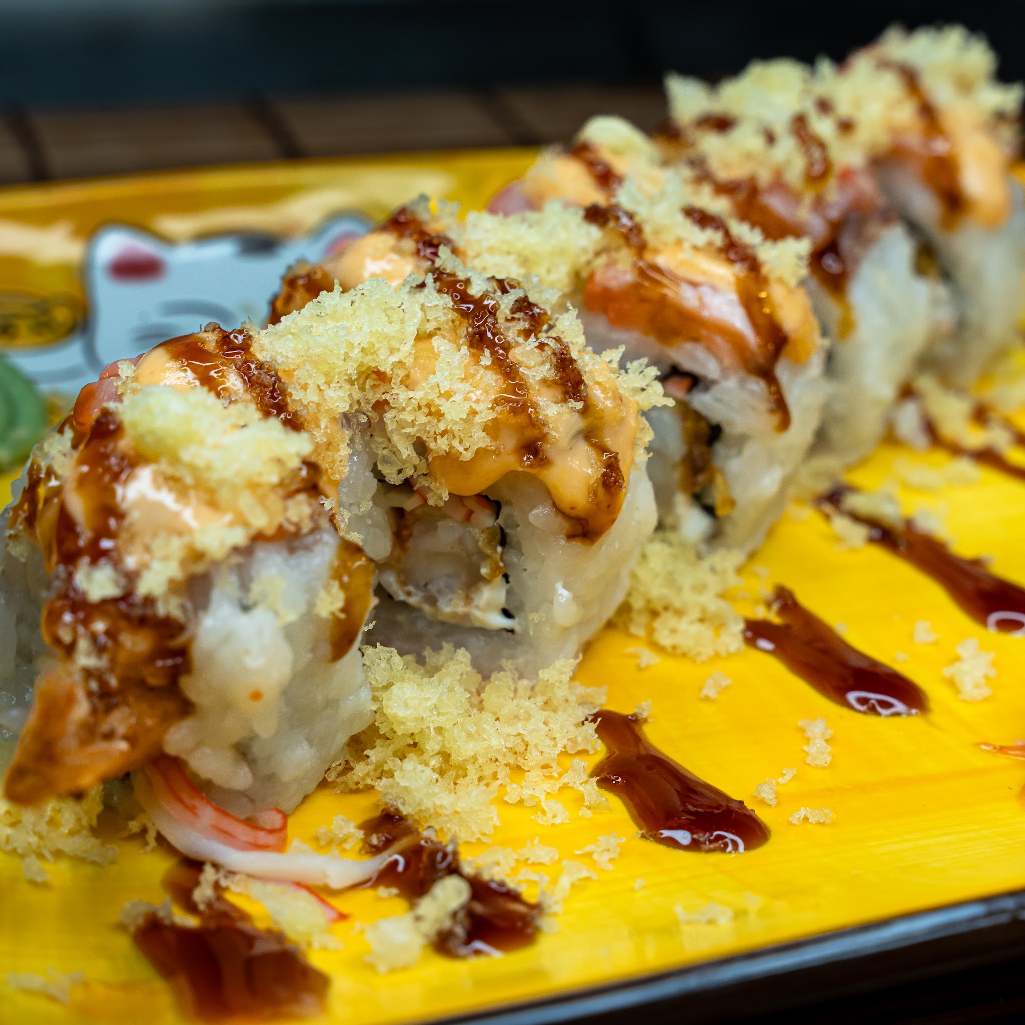 Sauced sushi rolls on a bright yellow serving board.