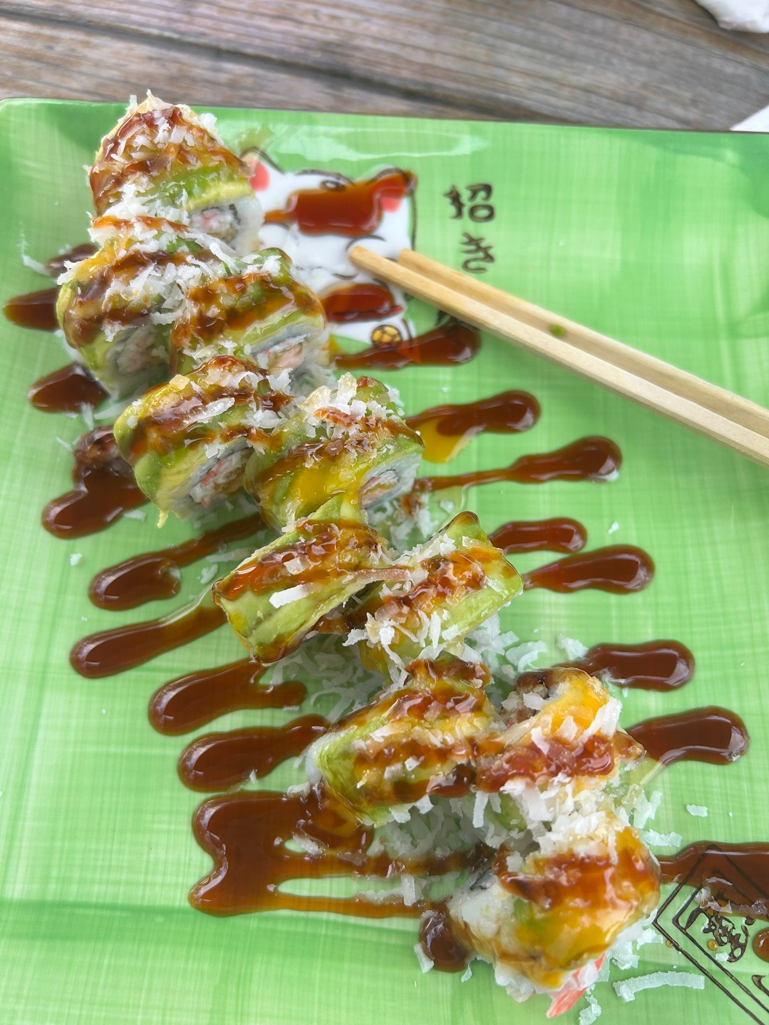 Sushi rolls topped with sauce on a green plate.