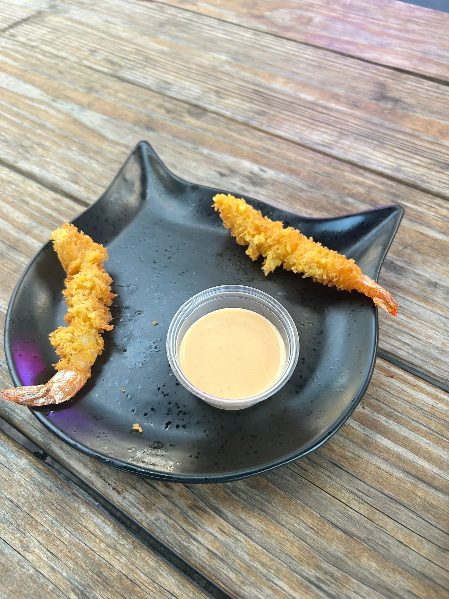 Breaded shrimp with dipping sauce on a black plate.